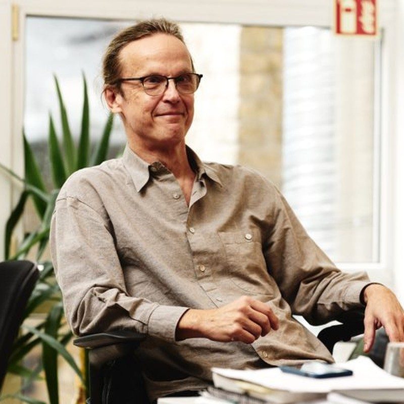 Alex Blumentals, seated by a window, in a light shirt and glasses