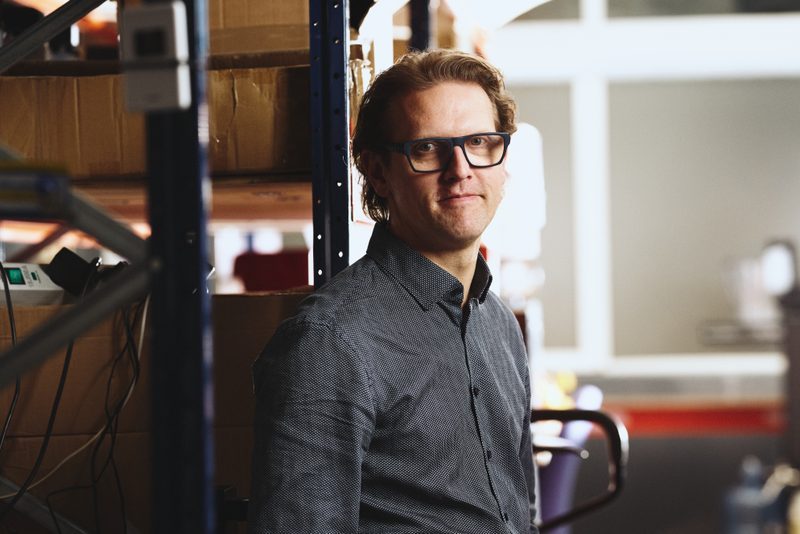 Edgars Rozentals in glasses and a dark shirt, standing among warehouse shelving
