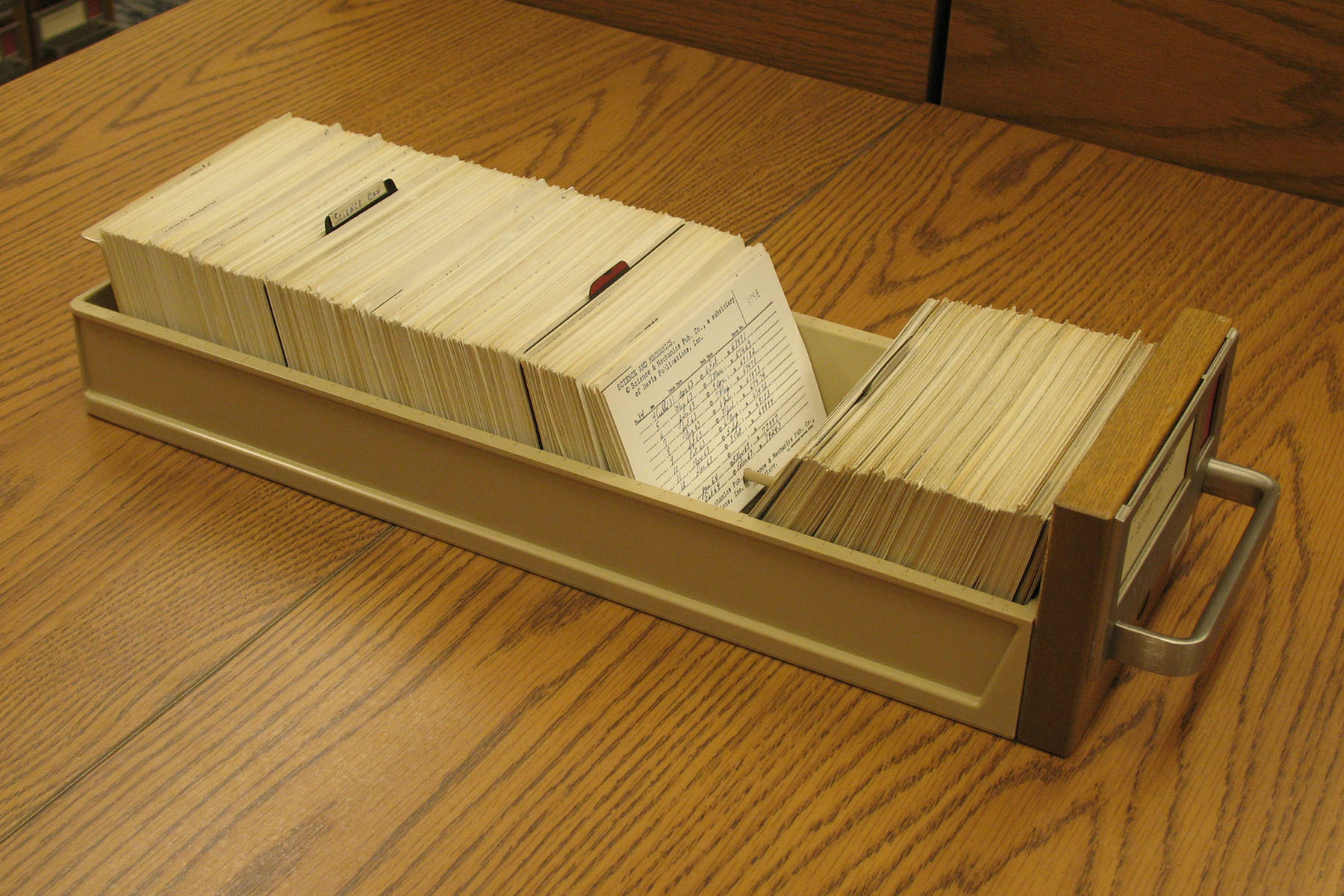 A drawer of index cards pulled from a card catalogue onto a wooden table