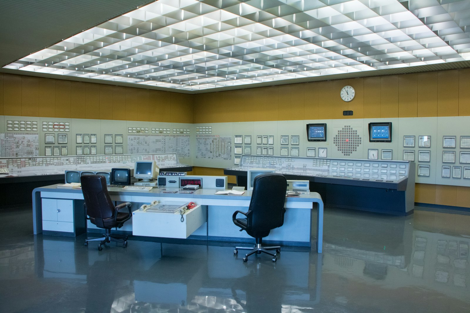 An empty industrial control room, operator chairs unattended before the panels