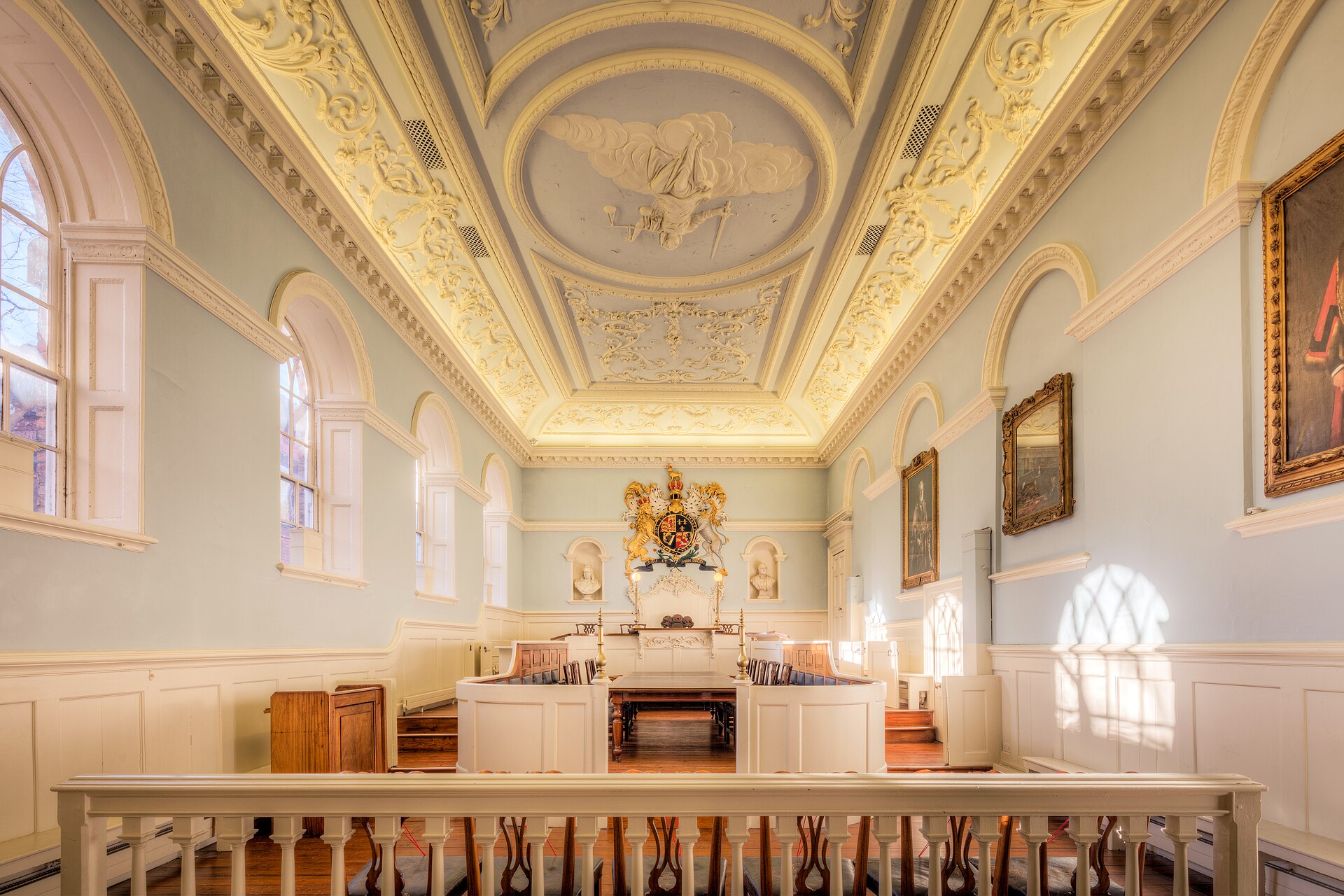 An empty eighteenth-century courtroom with a plaster ceiling, the royal arms above the bench