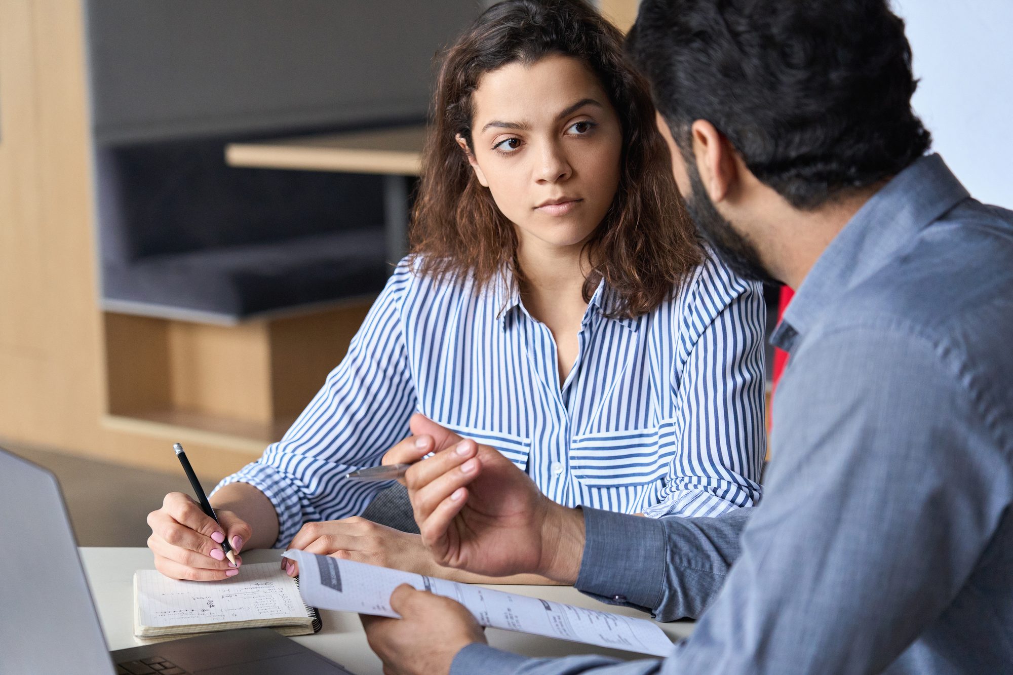 A young woman taking notes while a senior colleague walks her through a document