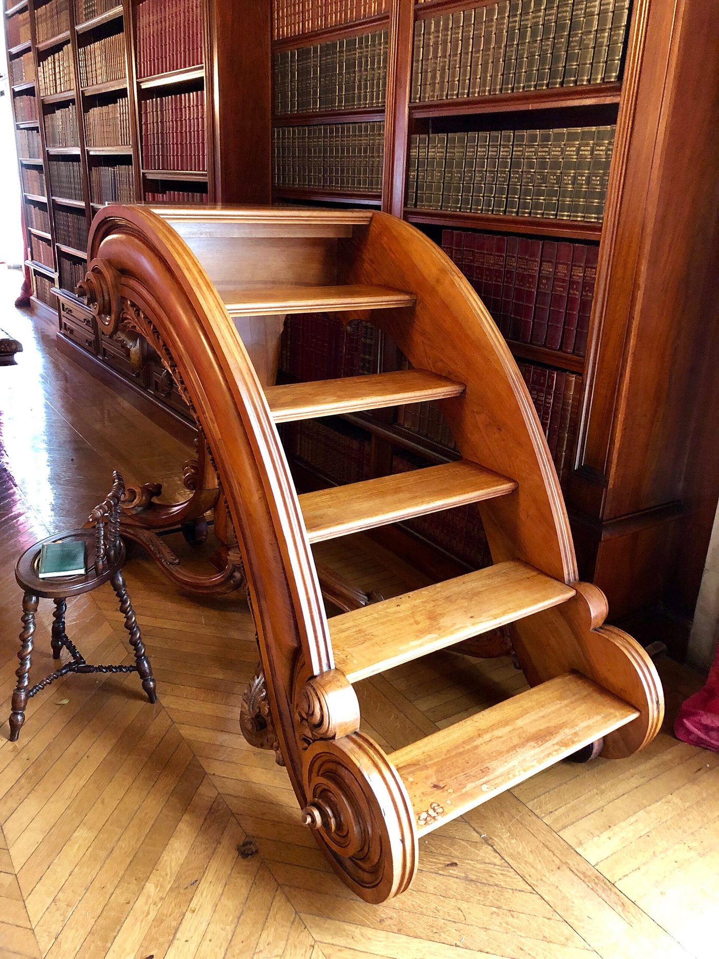 A curved wooden library ladder against shelves of leather-bound books